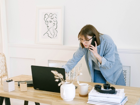 Focused woman on phone, researching on laptop, epitomizing diligent learning from top real estate blogs.